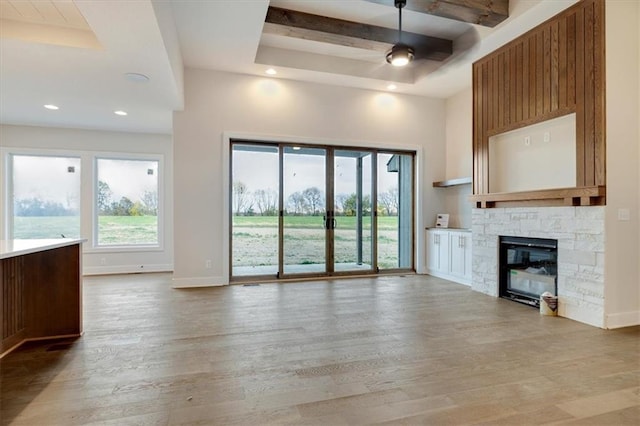 unfurnished living room featuring beam ceiling, a stone fireplace, and wood-type flooring