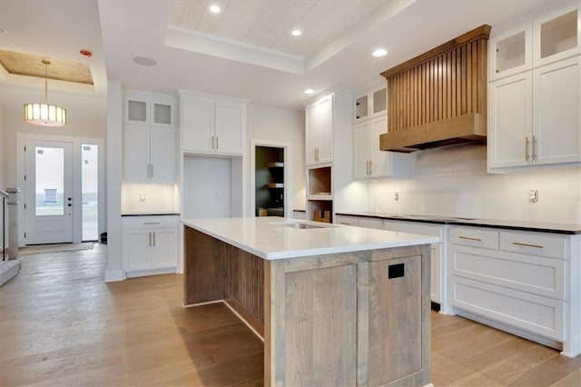 kitchen with a kitchen island, a tray ceiling, hanging light fixtures, light hardwood / wood-style floors, and white cabinets