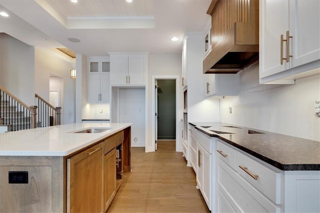 kitchen with a center island with sink, white cabinets, custom range hood, and light wood-type flooring