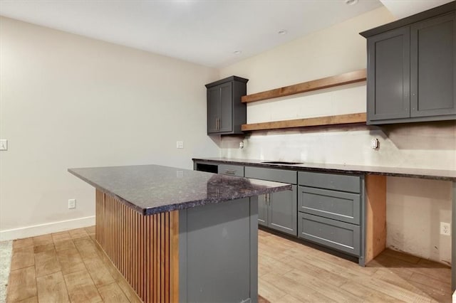 kitchen featuring built in desk, a kitchen island, dark stone counters, light wood-type flooring, and gray cabinetry