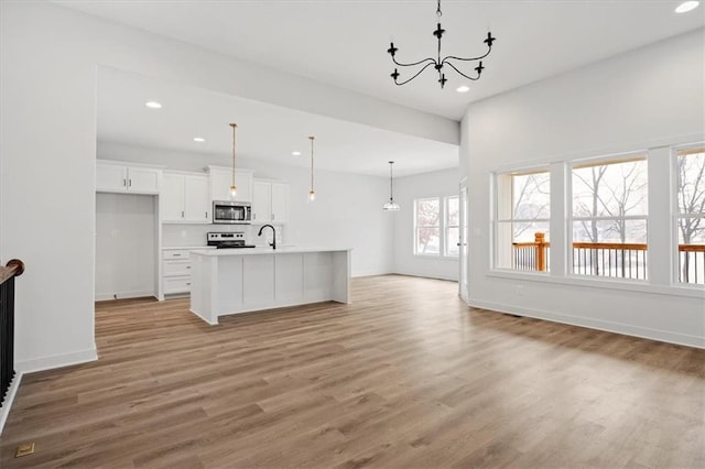 kitchen featuring electric range, white cabinetry, a kitchen island with sink, light wood-type flooring, and decorative light fixtures