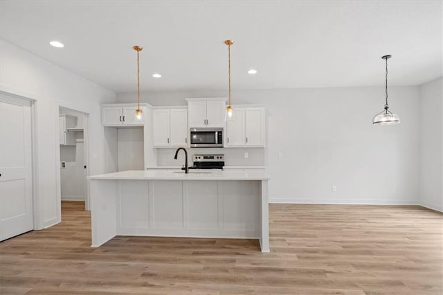 kitchen featuring white cabinets, an island with sink, light hardwood / wood-style flooring, pendant lighting, and stainless steel appliances