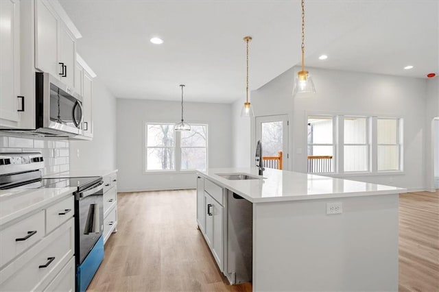 kitchen featuring sink, white cabinetry, stainless steel appliances, pendant lighting, and a center island with sink