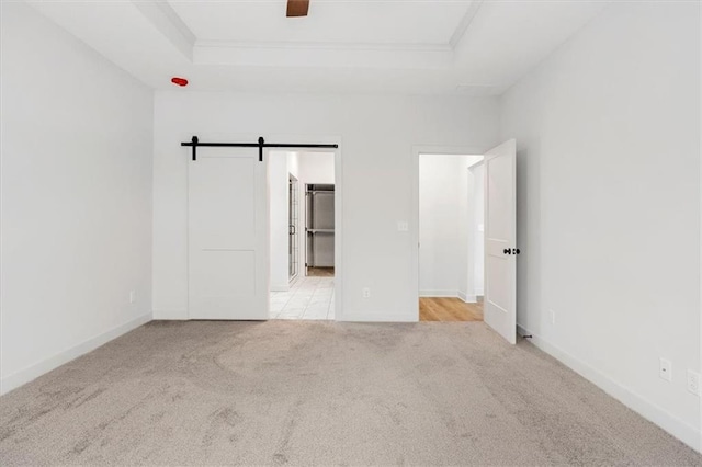 carpeted empty room featuring a barn door and a tray ceiling