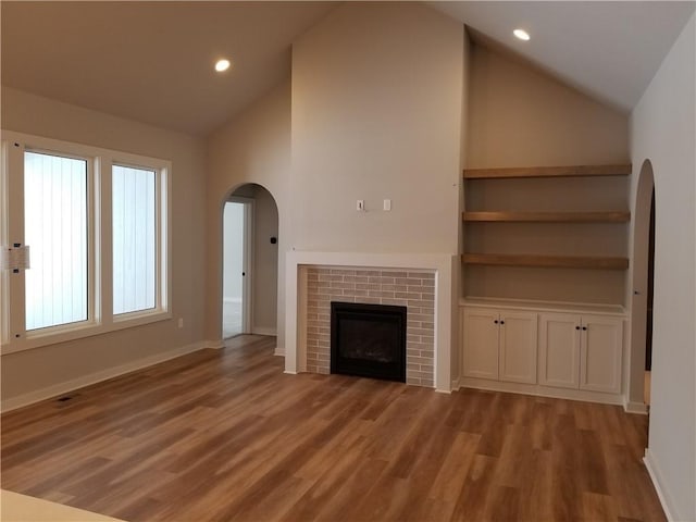 unfurnished living room featuring a brick fireplace, high vaulted ceiling, light hardwood / wood-style floors, and built in features