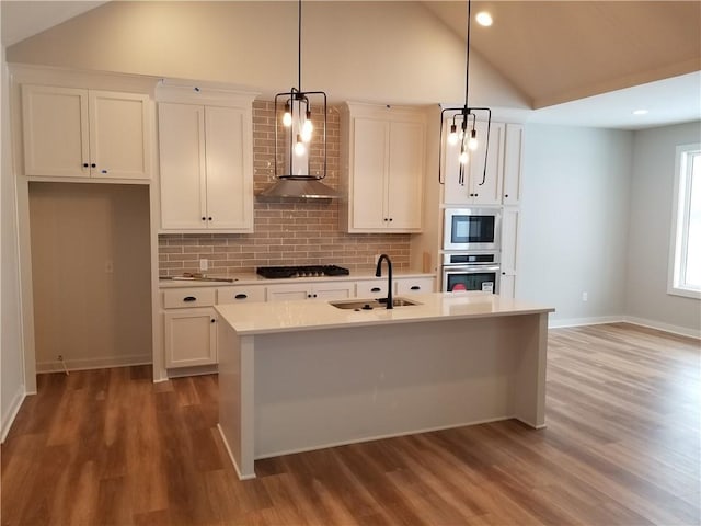 kitchen featuring stainless steel oven, hanging light fixtures, a center island with sink, and sink