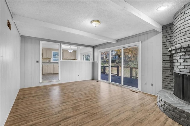 unfurnished living room with beamed ceiling, light wood-type flooring, a textured ceiling, and a brick fireplace