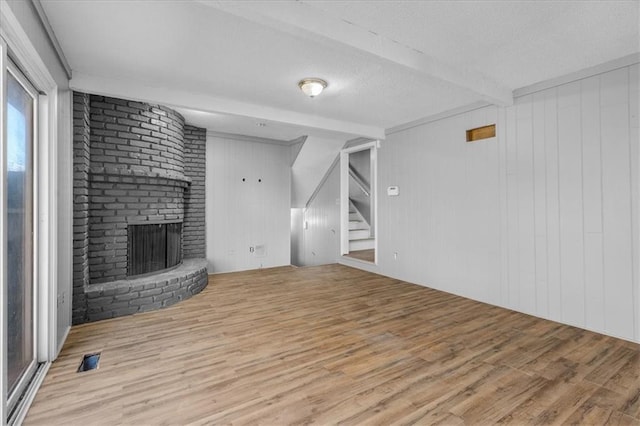 unfurnished living room featuring a fireplace, wooden walls, light hardwood / wood-style flooring, and beamed ceiling