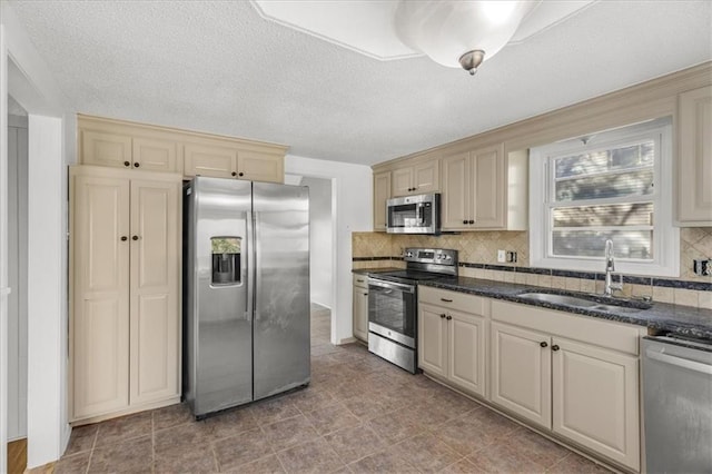 kitchen featuring decorative backsplash, appliances with stainless steel finishes, cream cabinetry, and sink