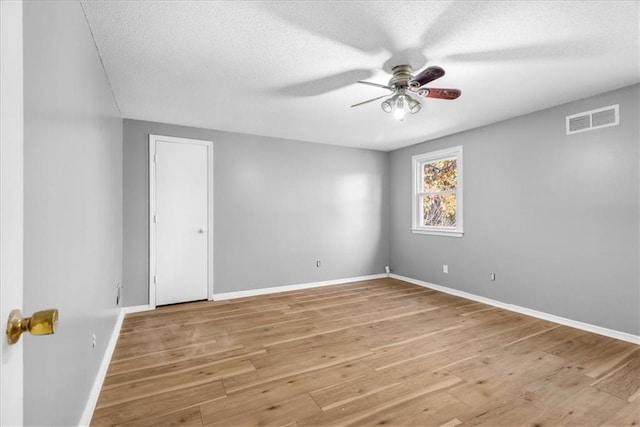 empty room with a textured ceiling, light wood-type flooring, and ceiling fan