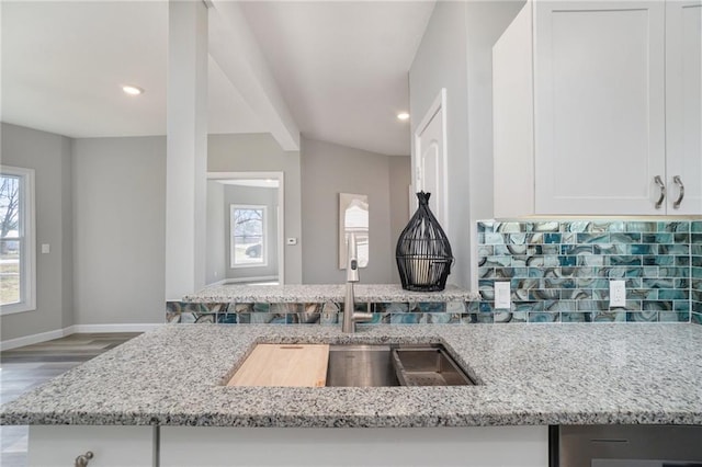 kitchen featuring white cabinets, light stone counters, hardwood / wood-style floors, and backsplash