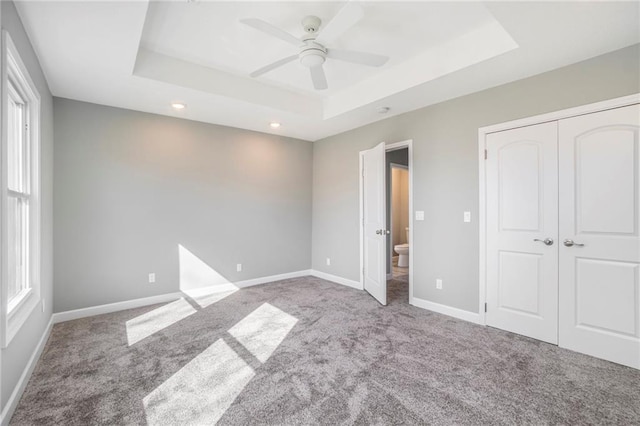 unfurnished bedroom featuring ceiling fan, a raised ceiling, and multiple windows