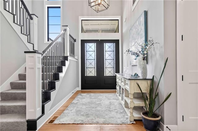 foyer entrance featuring a towering ceiling, a chandelier, french doors, and wood-type flooring