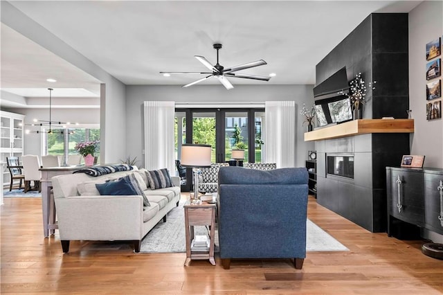 living room with ceiling fan with notable chandelier, french doors, a tile fireplace, and light hardwood / wood-style flooring