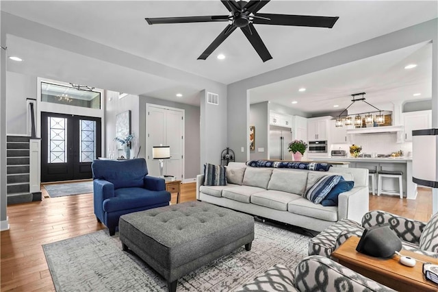 living room featuring ceiling fan with notable chandelier and light hardwood / wood-style flooring