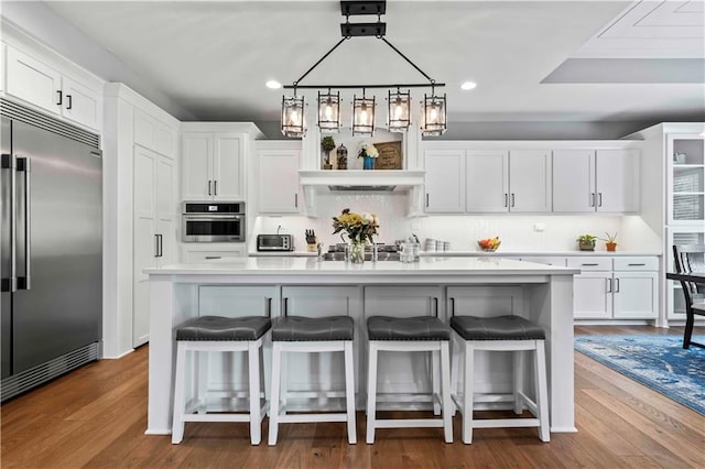 kitchen with appliances with stainless steel finishes, an island with sink, white cabinets, and wood-type flooring