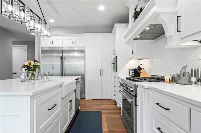 kitchen with high quality appliances, white cabinetry, premium range hood, and an island with sink