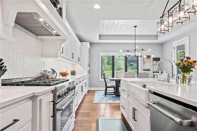 kitchen featuring stainless steel appliances, custom range hood, white cabinets, light hardwood / wood-style flooring, and decorative light fixtures