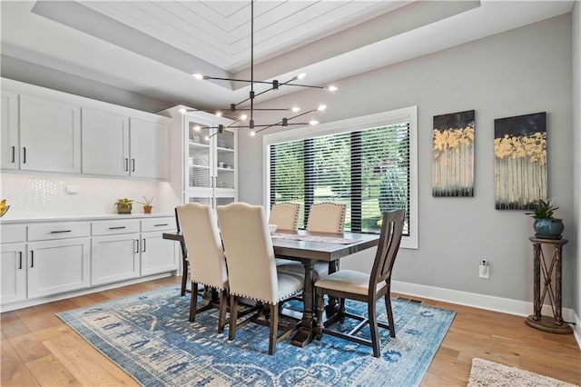 dining space featuring light wood-type flooring, a tray ceiling, and a chandelier