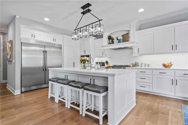 kitchen with a center island with sink, white cabinets, built in refrigerator, and hanging light fixtures