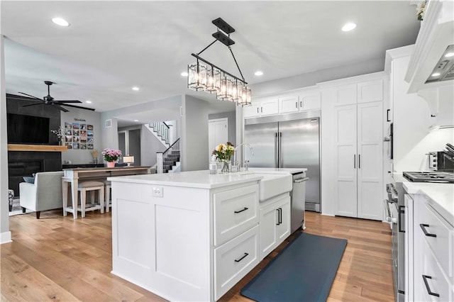 kitchen featuring ceiling fan with notable chandelier, high end appliances, white cabinets, and a kitchen island with sink