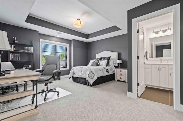 bedroom with ensuite bath, light colored carpet, a tray ceiling, and sink