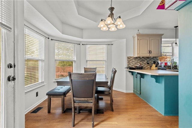 dining space featuring a chandelier, light hardwood / wood-style flooring, and a raised ceiling