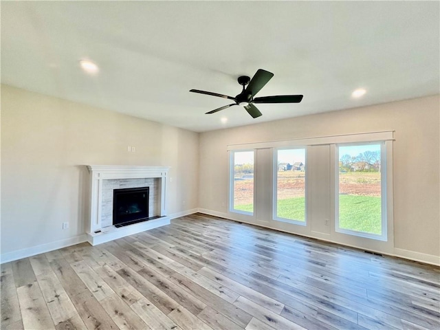 unfurnished living room with ceiling fan, a tile fireplace, and light wood-type flooring