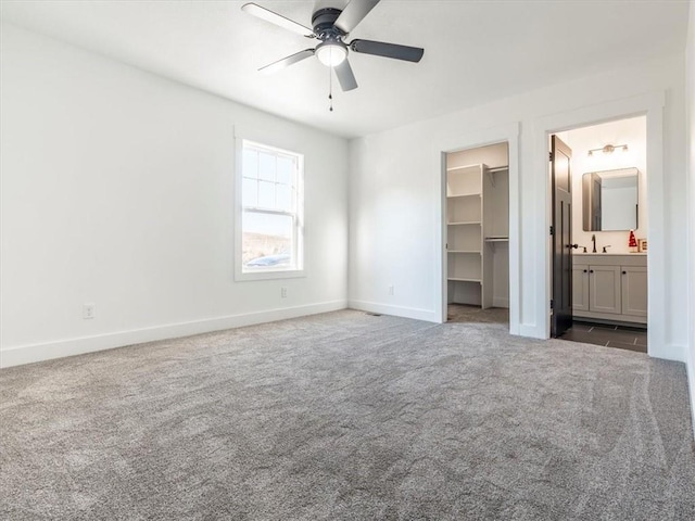 unfurnished bedroom featuring dark colored carpet, ensuite bathroom, ceiling fan, a spacious closet, and a closet