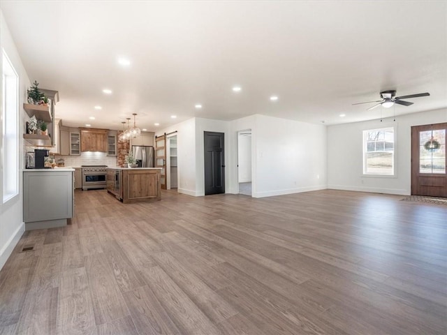 unfurnished living room with a barn door, light hardwood / wood-style flooring, and ceiling fan