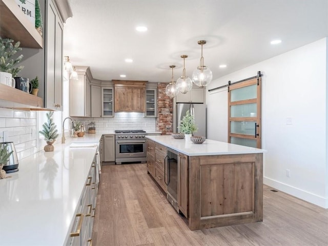 kitchen featuring appliances with stainless steel finishes, light wood-type flooring, a spacious island, sink, and a barn door