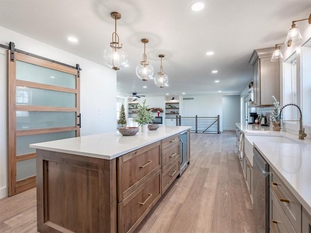 kitchen featuring a barn door, light hardwood / wood-style flooring, stainless steel dishwasher, decorative light fixtures, and a kitchen island