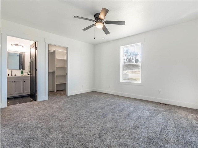 unfurnished bedroom with ceiling fan, dark carpet, a spacious closet, and connected bathroom