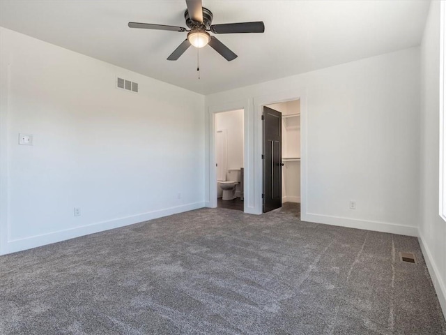 unfurnished bedroom featuring a walk in closet, ceiling fan, dark colored carpet, connected bathroom, and a closet