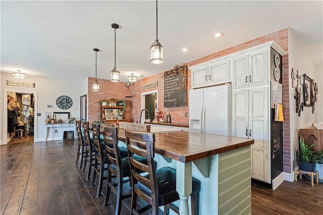 kitchen with a center island, white fridge with ice dispenser, butcher block countertops, decorative light fixtures, and brick wall