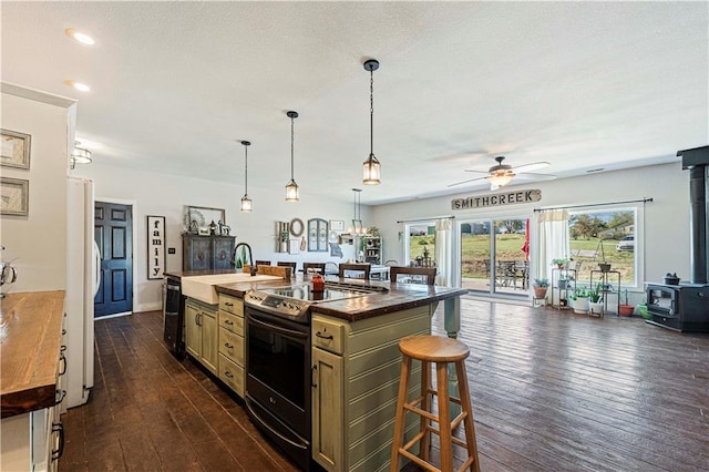 kitchen featuring a wood stove, dark hardwood / wood-style flooring, an island with sink, a breakfast bar area, and black appliances