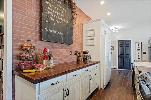 kitchen featuring butcher block counters, electric range, white fridge with ice dispenser, dark wood-type flooring, and brick wall