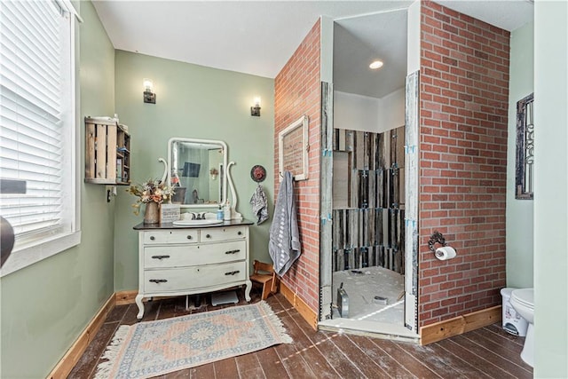 bathroom featuring vanity, a shower, toilet, wood-type flooring, and brick wall