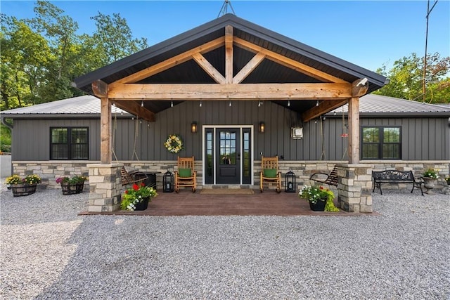 doorway to property featuring a deck, board and batten siding, stone siding, and metal roof