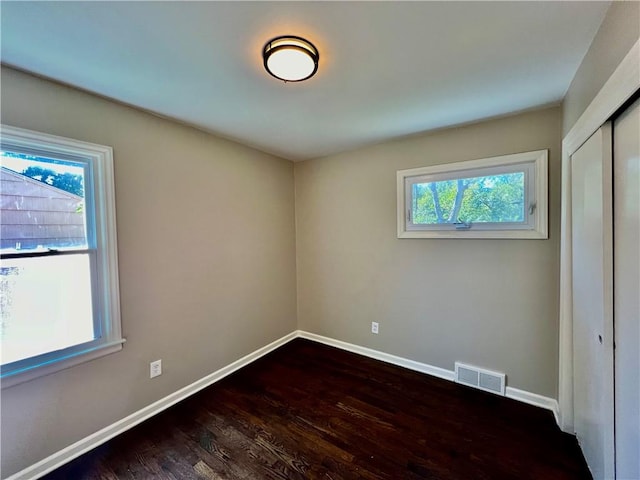 empty room featuring plenty of natural light and dark wood-type flooring