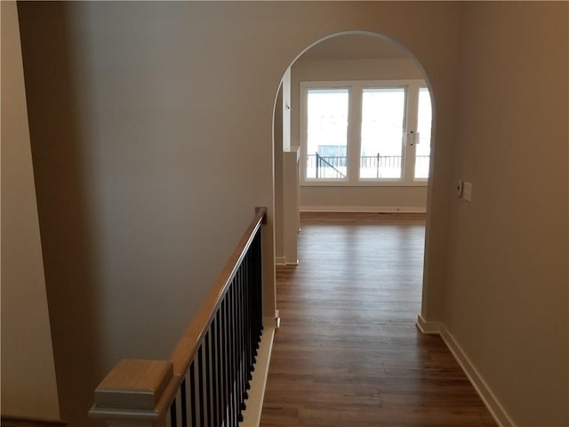 corridor with baseboards, arched walkways, and dark wood-type flooring