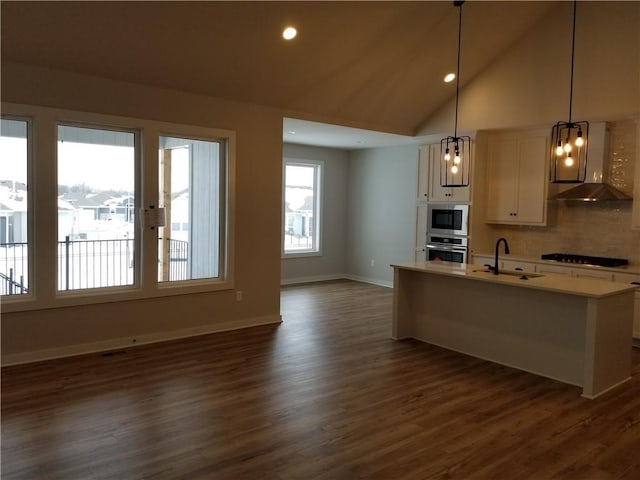 kitchen with stainless steel appliances, light countertops, vaulted ceiling, a sink, and wall chimney range hood