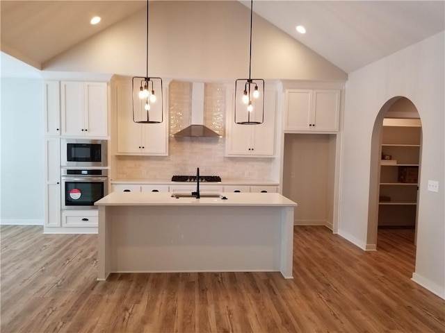 kitchen featuring decorative light fixtures, stainless steel appliances, light countertops, wall chimney range hood, and a sink