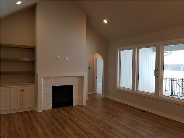 unfurnished living room with arched walkways, a fireplace, vaulted ceiling, wood finished floors, and baseboards