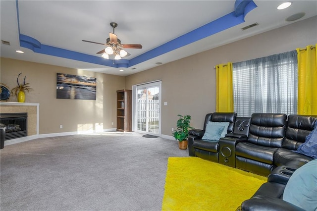 living room with a raised ceiling, ceiling fan, and carpet flooring