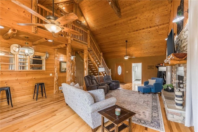 living room with ceiling fan, wooden ceiling, beamed ceiling, light hardwood / wood-style floors, and a stone fireplace