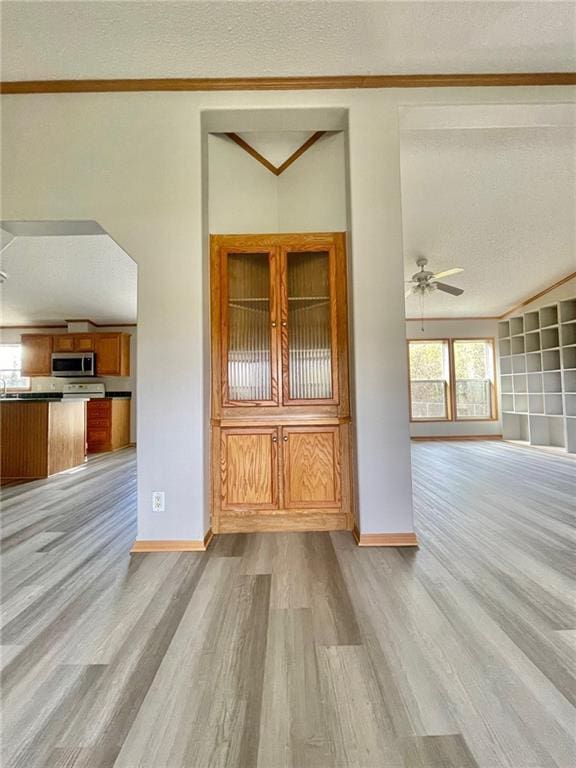 unfurnished living room featuring ceiling fan, light hardwood / wood-style floors, crown molding, and a textured ceiling