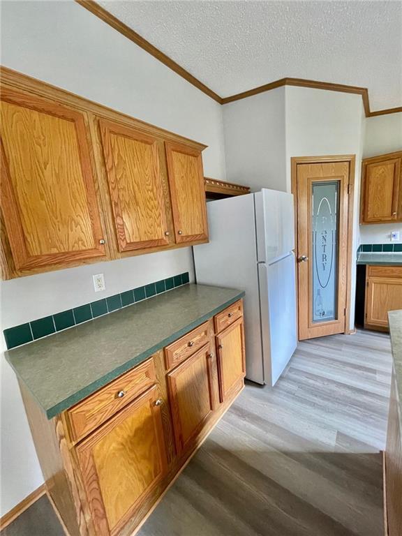 kitchen featuring white fridge, light hardwood / wood-style floors, a textured ceiling, and ornamental molding