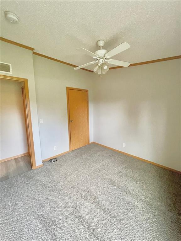 unfurnished bedroom featuring ceiling fan, carpet floors, a textured ceiling, and ornamental molding