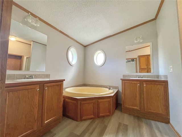 bathroom with a bathing tub, vanity, a textured ceiling, hardwood / wood-style floors, and lofted ceiling